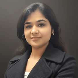 A smiling woman wearing a black blazer, standing in front of a grey background.
